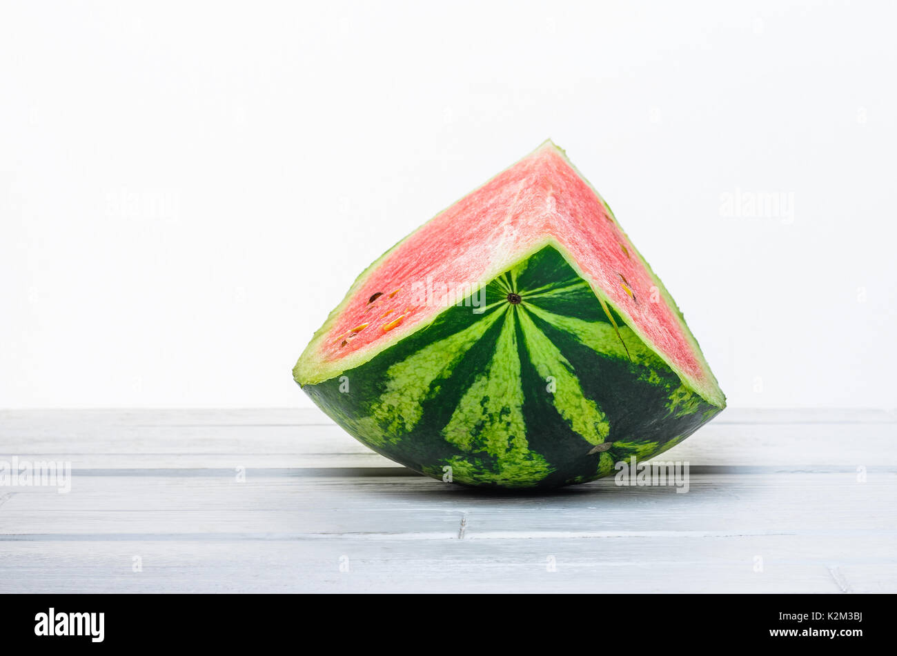 Scheibe einer Wassermelone auf weissem Holztisch auf weißem Hintergrund. Minimalistische leere Hintergrund Stockfoto