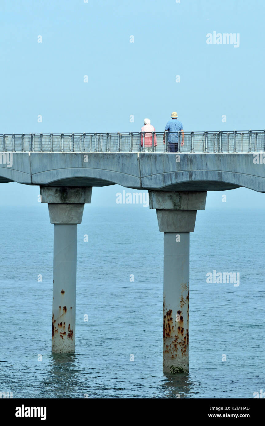Ein pensionierter ältere ältere Paar entlang eine Brücke weg Hand in Hand über das Meer an der Küste im Urlaub bleiben aktiv in den Ruhestand Stockfoto