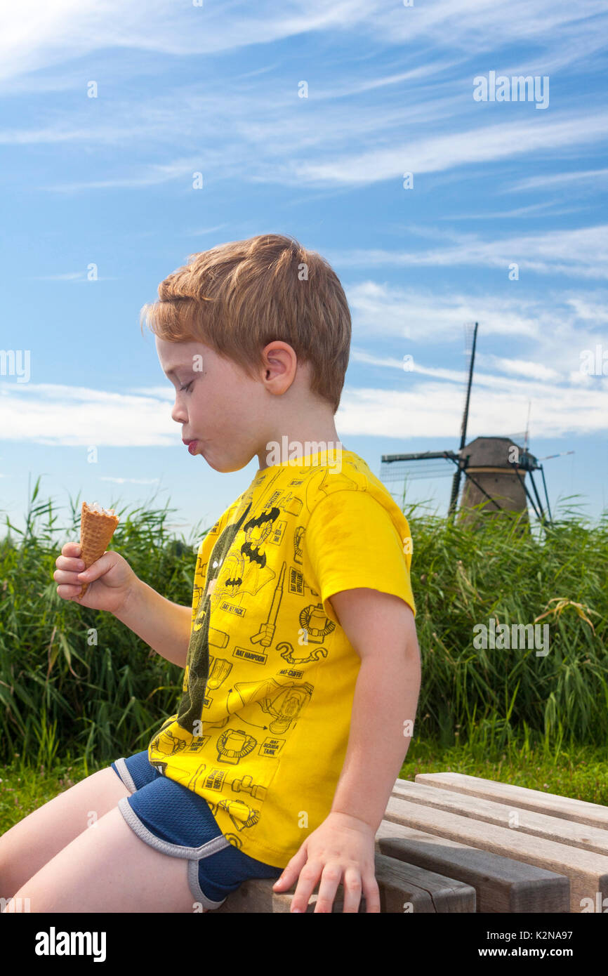 Ein Junge essen ein Eis mit einem traditionellen holländischen Windmühle im Hintergrund. Kinderdijk, Niederlande Stockfoto