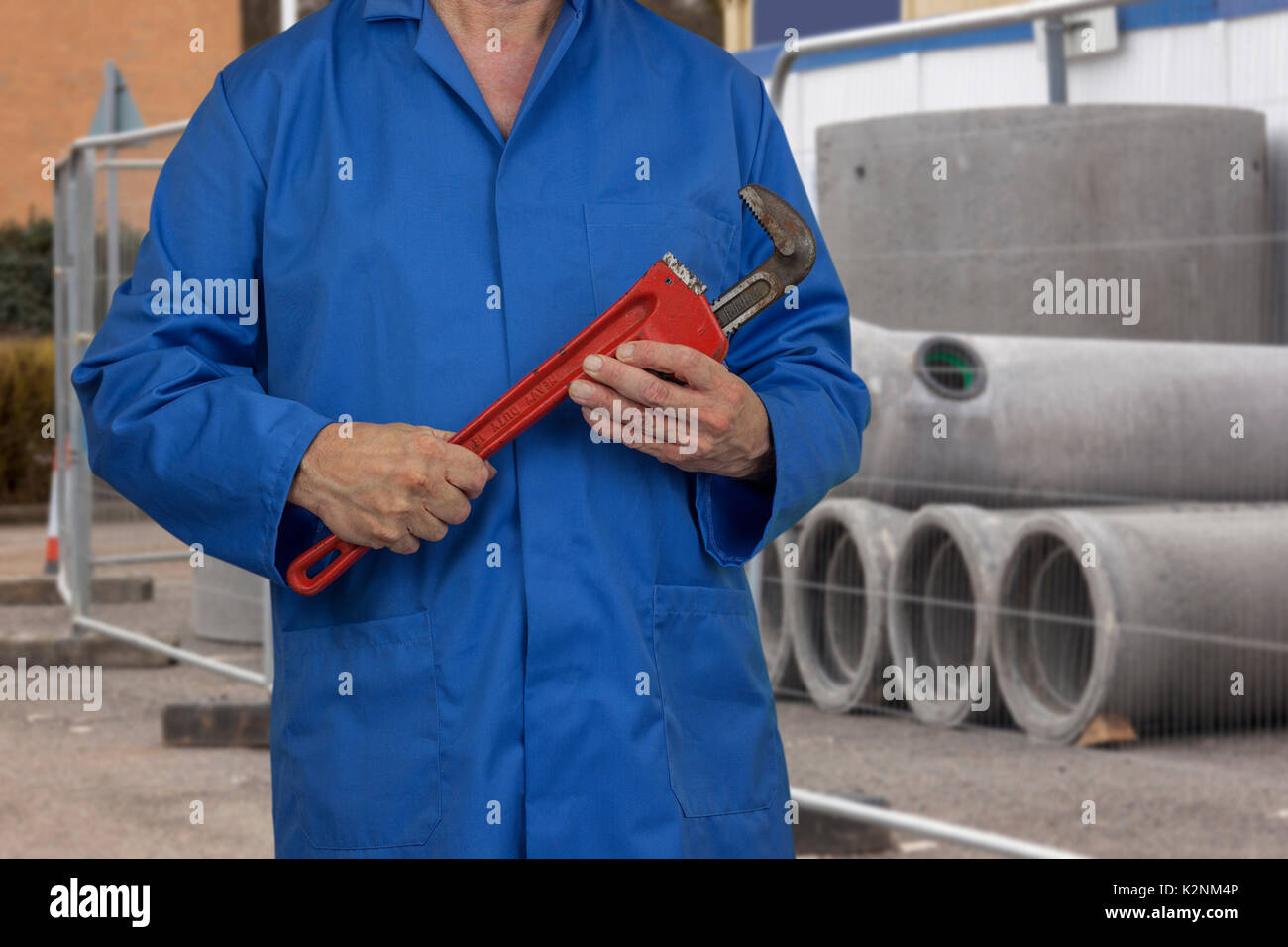 Klempner in blauen Overalls einstellen einen Schlüssel beim Stehen vor einem Stapel von konkreten Ablassrohre auf einer Baustelle Stockfoto