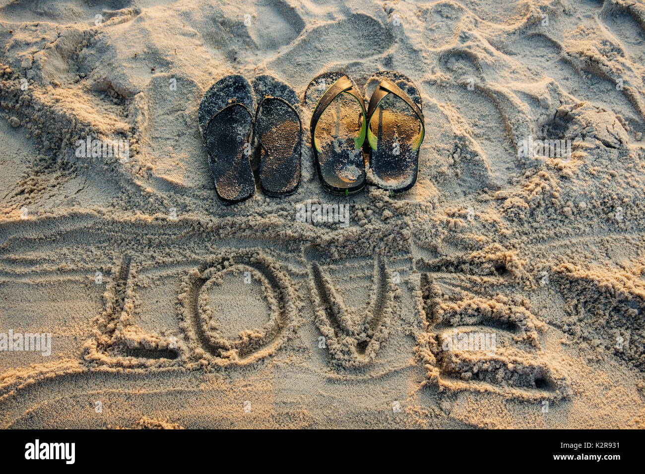 Sand Schreiben der Liebe Wort mit ein Paar Sandalen am Strand Stockfoto