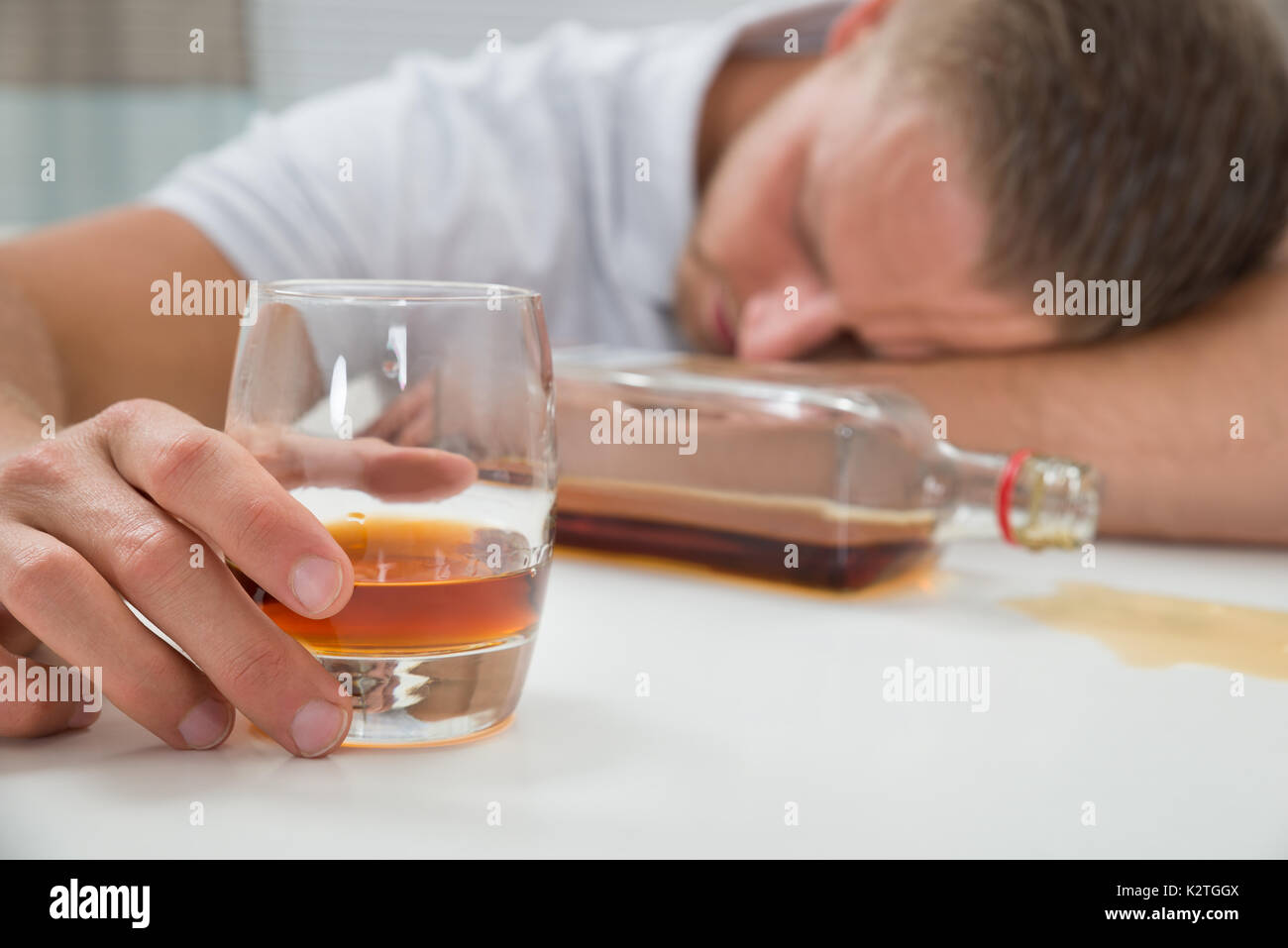Junge betrunkene Menschen schlafen auf Tisch mit einem Glas Schnaps Stockfoto