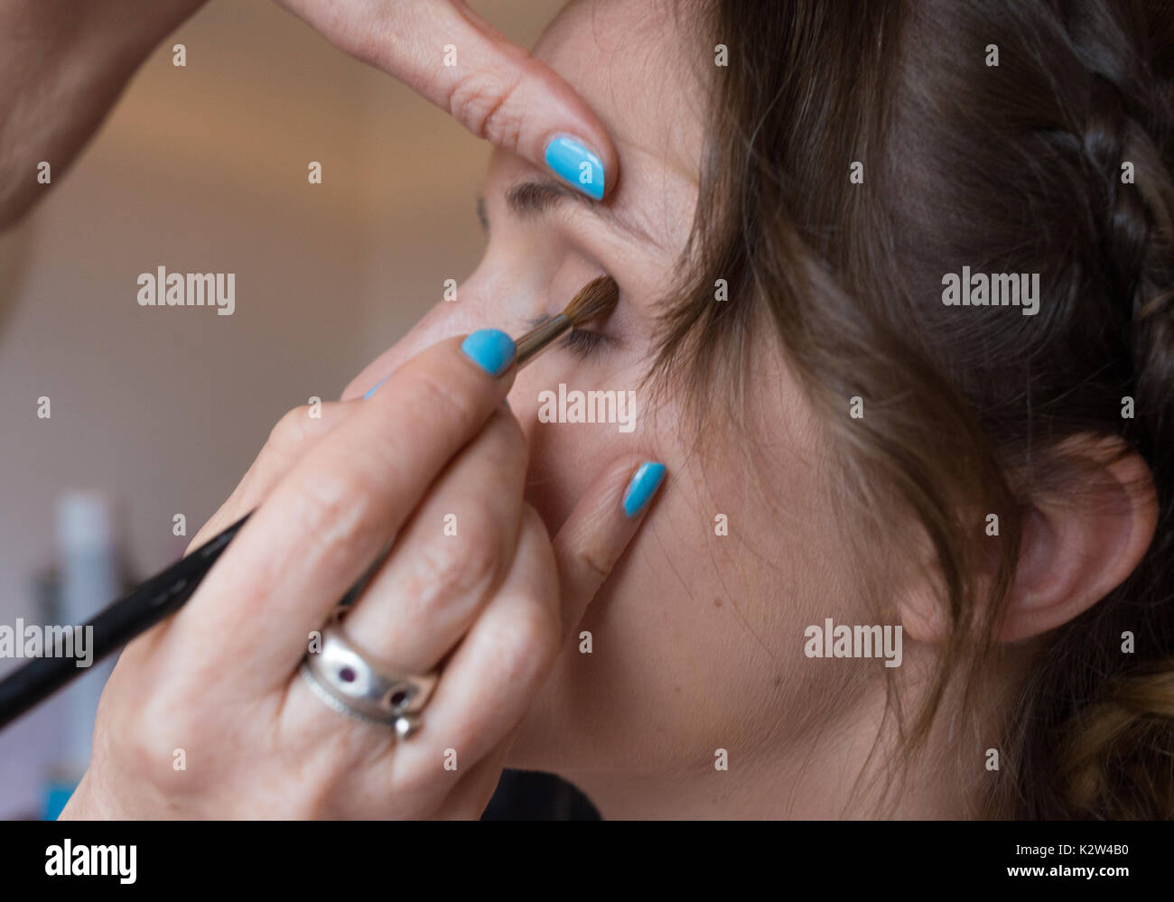 Eine junge Frau, die sich ein lidschatten Anwendung von einem professionellen Make up artist mit Licht blau lackierte Fingernägel. Stockfoto