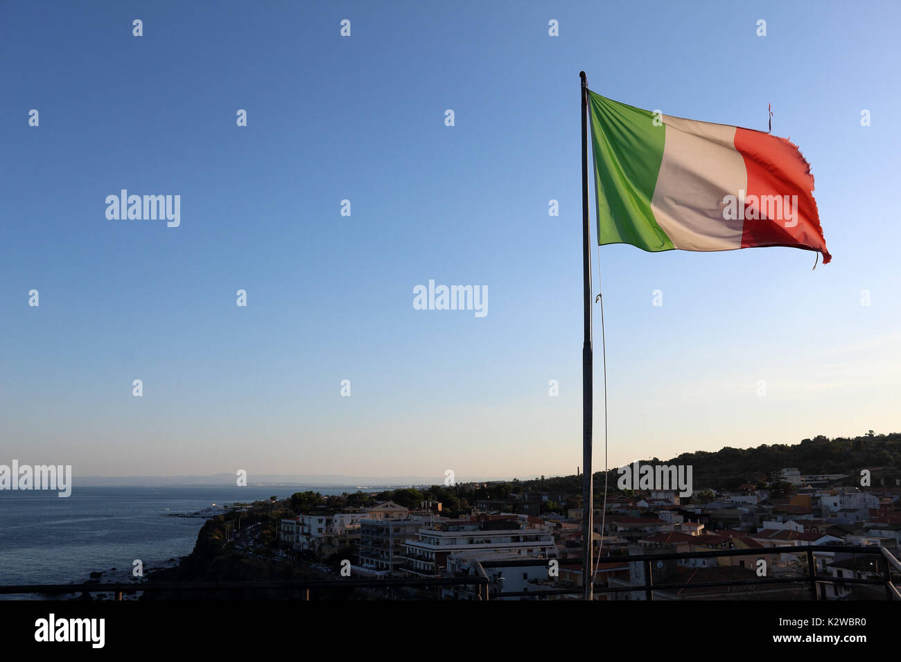Italienische Flagge über eine Stadt im Sommer fliegen, mit klaren, blauen Himmel hinter. Aci Castello, Sizilien. Stockfoto