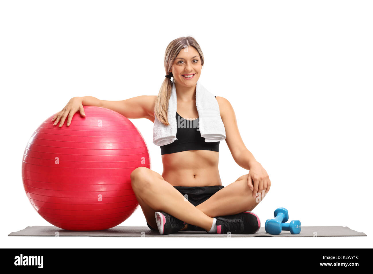 Junge Frau mit einem Pilates Ball und Hanteln sitzen auf einer Gymnastikmatte auf weißem Hintergrund Stockfoto