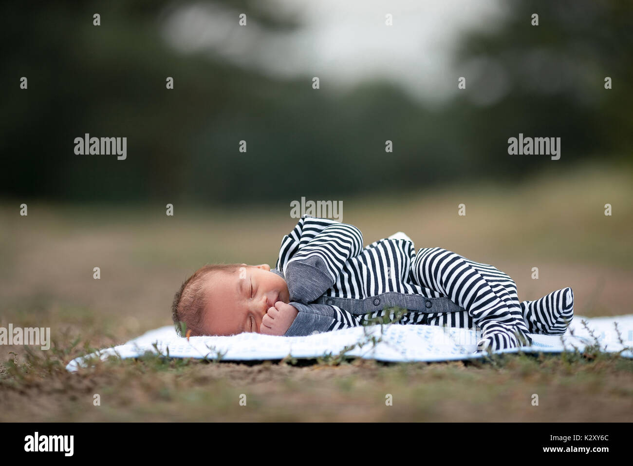Neugeborenes im gestreiften Strampelanzug schläft auf blaue Bettdecke auf Gras im Park. Kopieren Platz oben. Stockfoto