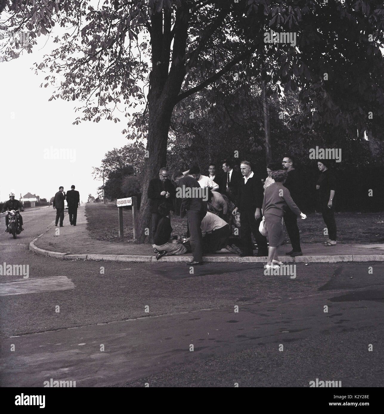 1960, historische, der allgemeinen Öffentlichkeit versammeln sich, um sich für einen verletzten Mann lag auf einem Bürgersteig durch eine Straße, England, UK. Stockfoto