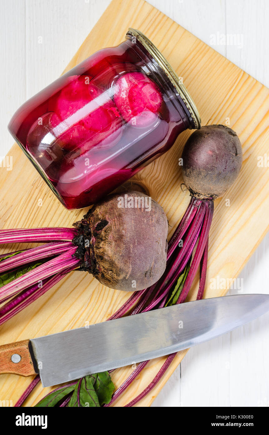 Glas Glas mit eingemachten Rüben hausgemacht und frisch Bio rote Rüben mit Haulm mit Schneidebrett und großen Messer auf einem weißen Holz- Hintergrund der Ansicht von oben. Rüben Stockfoto