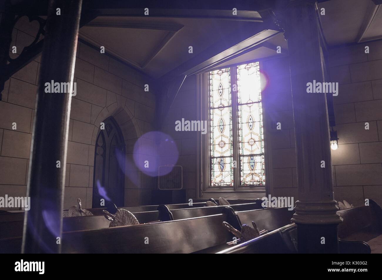 Sun Filter durch die Glasmalerei von einer alten Kirche, Erstellen von Schatten auf die Bänke mit gewebten Fans in ihren Halterungen, Baltimore, Maryland, September, 2013. Stockfoto