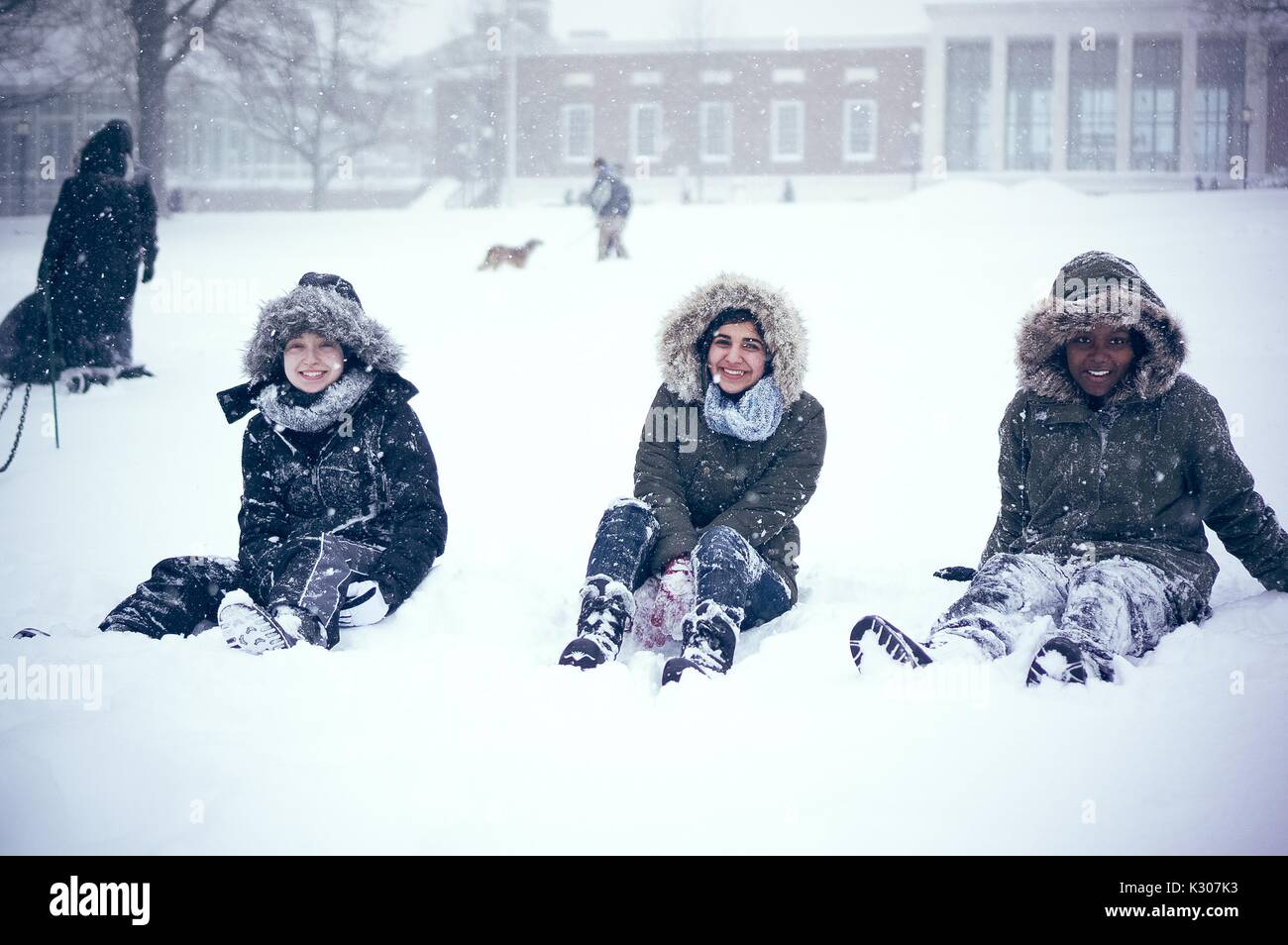 Drei Studenten tragen mit Kapuze Schnee gang Lächeln und für ihre Foto posieren, während Lounging im Schnee während einer Snow Day an der Johns Hopkins University, Baltimore, Maryland, 2016. Stockfoto