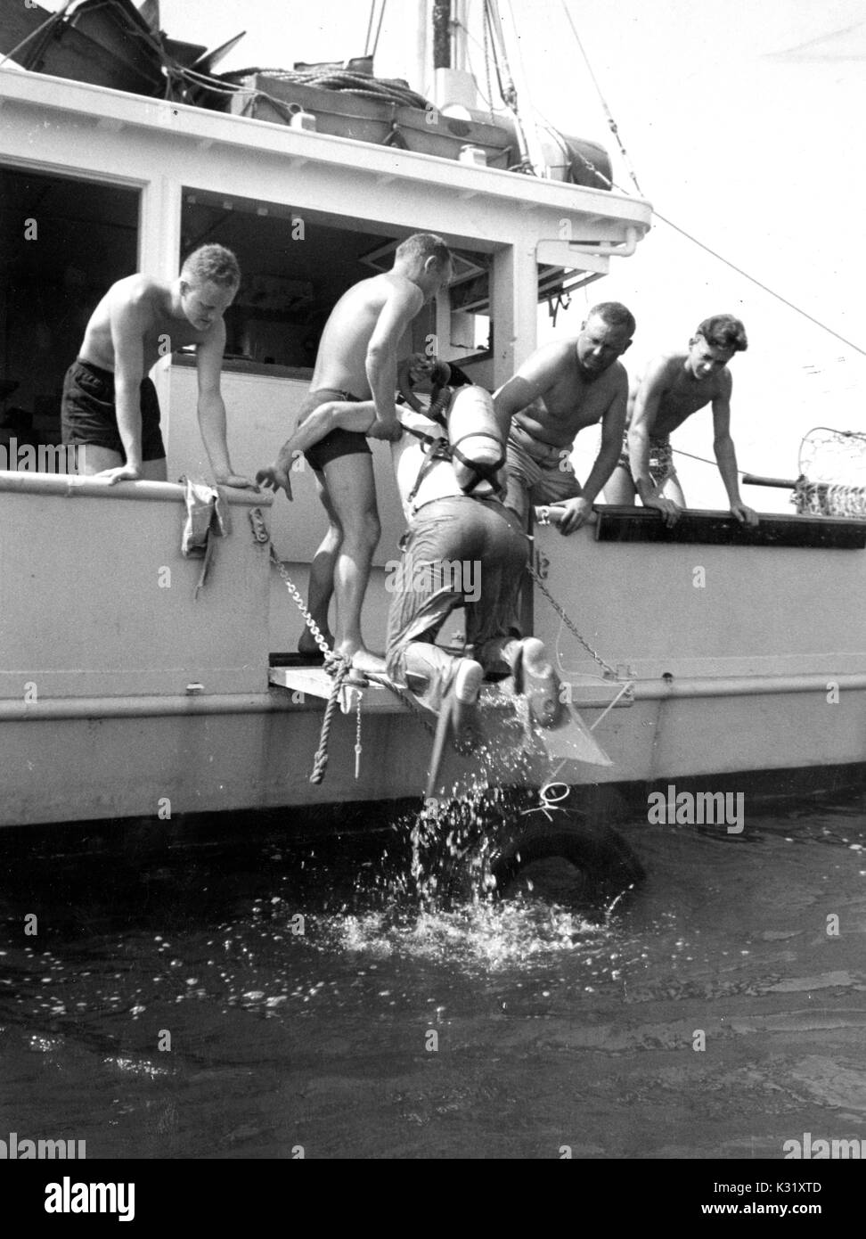 Vier Wissenschaftler in Badehose über den Rand des Bootes bis ein Taucher aus dem Wasser an einem hellen Sommertag zu helfen, lehnend, an Bord der Maury Forschungsschiff für die Chesapeake Bay Institut, 1952. Stockfoto