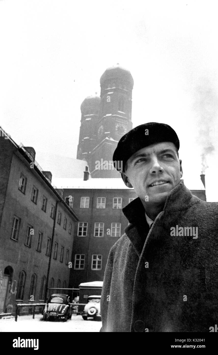 Candid Foto von John Richard Cary, Professor für Deutsche Literatur an der Johns Hopkins University und der brennenden Quaker, vor einer verschneiten Frauenkirche, eine Katholische Kathedrale in München Sterben stehend, trägt einen wollmantel und Baskenmütze, lächelnd, während sie mit dem Abstand, München, Deutschland, März 1954 blicken. Stockfoto