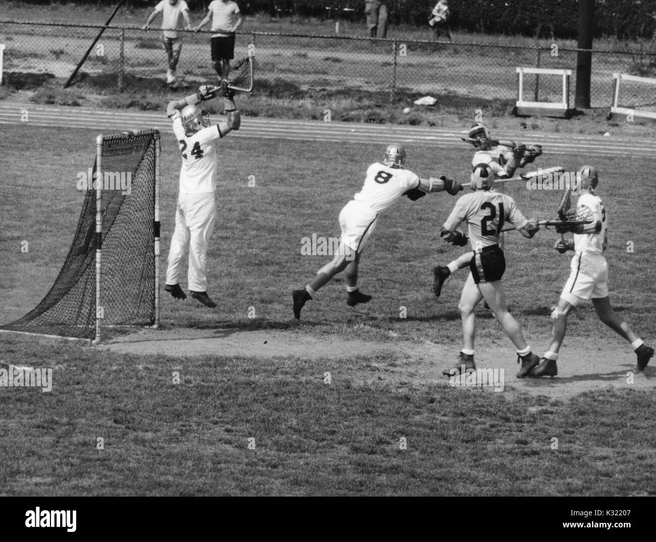 Graustufen Aktion Foto während einen Men's lacrosse Übereinstimmung zwischen der Johns Hopkins University und der United States Military Academy in West Point, während Micky Webster Nummer 10 von JHU schießt den Ball über seine Schulter, wodurch goalie und Verteidigung Mitglied aus der Armee in die Luft zu springen, um den Schuß zu blockieren, mit John jory Nummer 21 von JHU läuft das Ziel, Baltimore, Maryland, 27. April 1957. Stockfoto