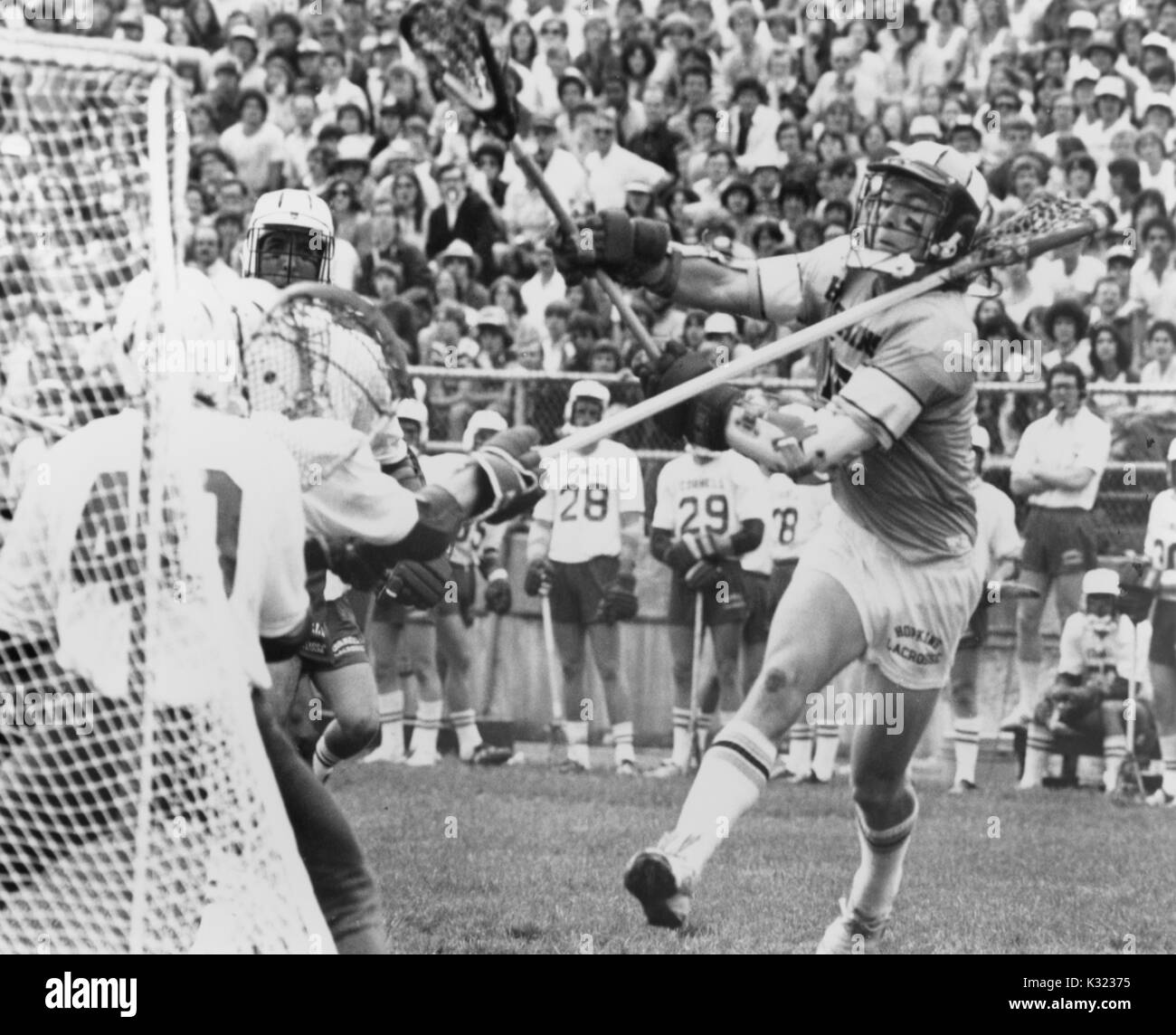 Graustufen Aktion Foto während der Johns Hopkins University Herren lacrosse Spiel gegen Cornell University, als JHU Spieler schleudert die Kugel aus seinem Stock einen Schuß gegen den Torwart, der mit seinem Stock hoch in die Luft zu nehmen, mit Spielern und überfüllt, steht gerade die spielen, Baltimore, Maryland, 27. Mai 1978. Stockfoto