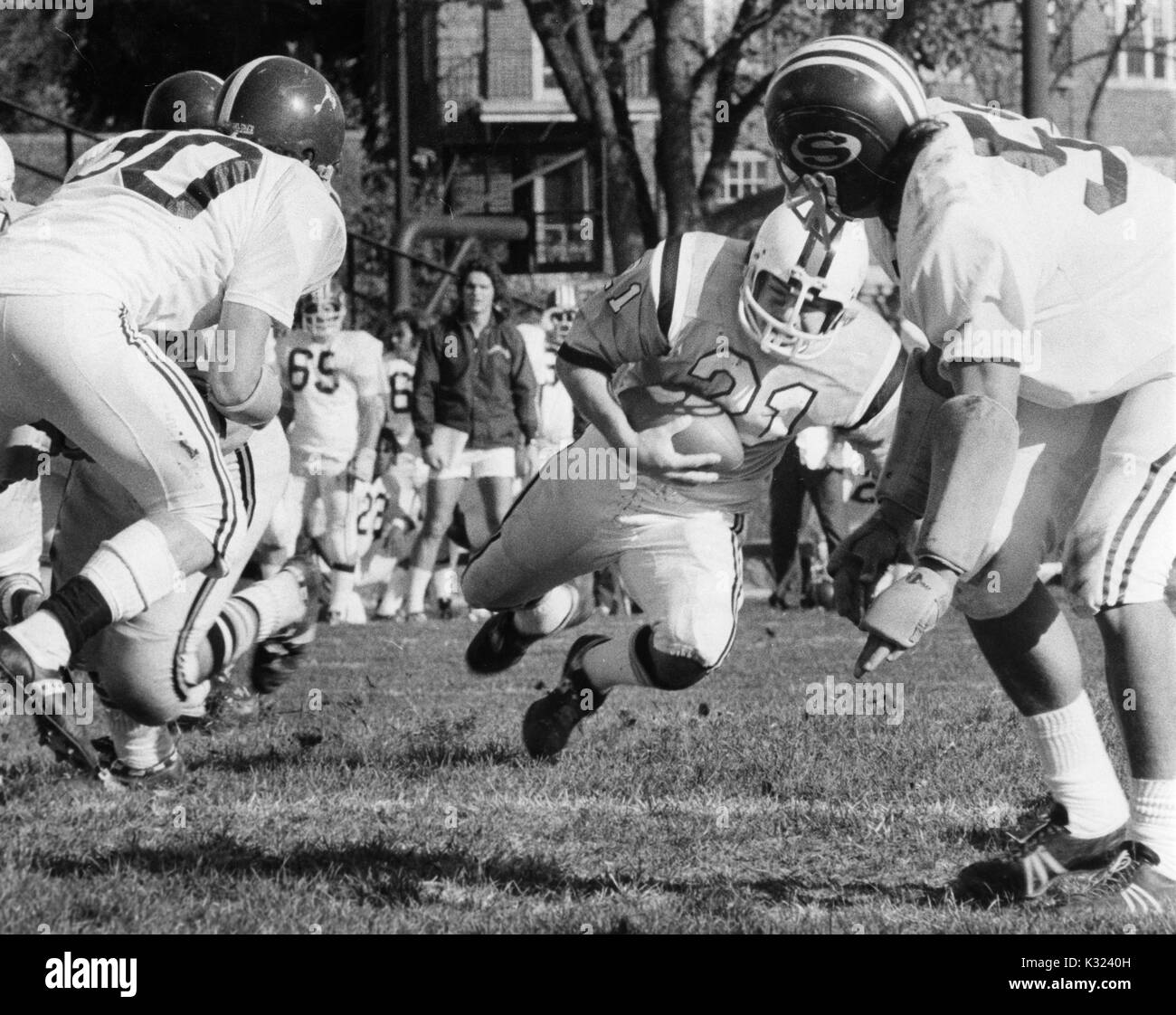 Ein Johns Hopkins football player bereitet zu fallen, die den Fußball mit eingehenden Spieler der gegnerischen Mannschaft eingehender mit der Hopkins Trainer und Spieler auf der Seite im Hintergrund an der Johns Hopkins University, Baltimore, Maryland, 1975 sichtbar. Stockfoto