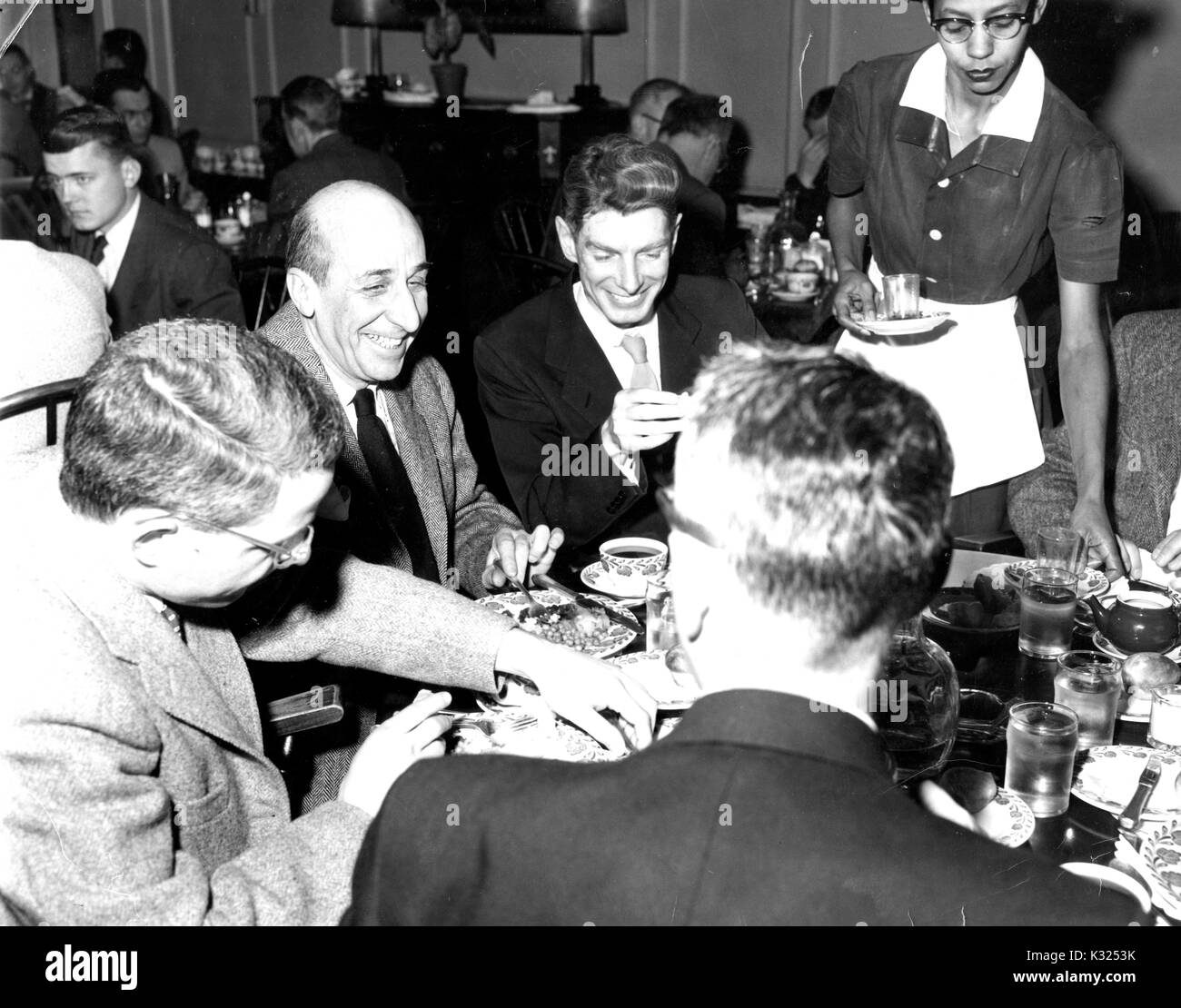 Bei einem Abendessen in der Johns Hopkins University Club Gebäude, männliche Mitglieder der Fakultät tragen Blazer Lächeln und Lachen rund um einen Esstisch, während eine weibliche Server erreicht eine Tasse Tee zu liefern, Baltimore, Maryland, 1955. Stockfoto
