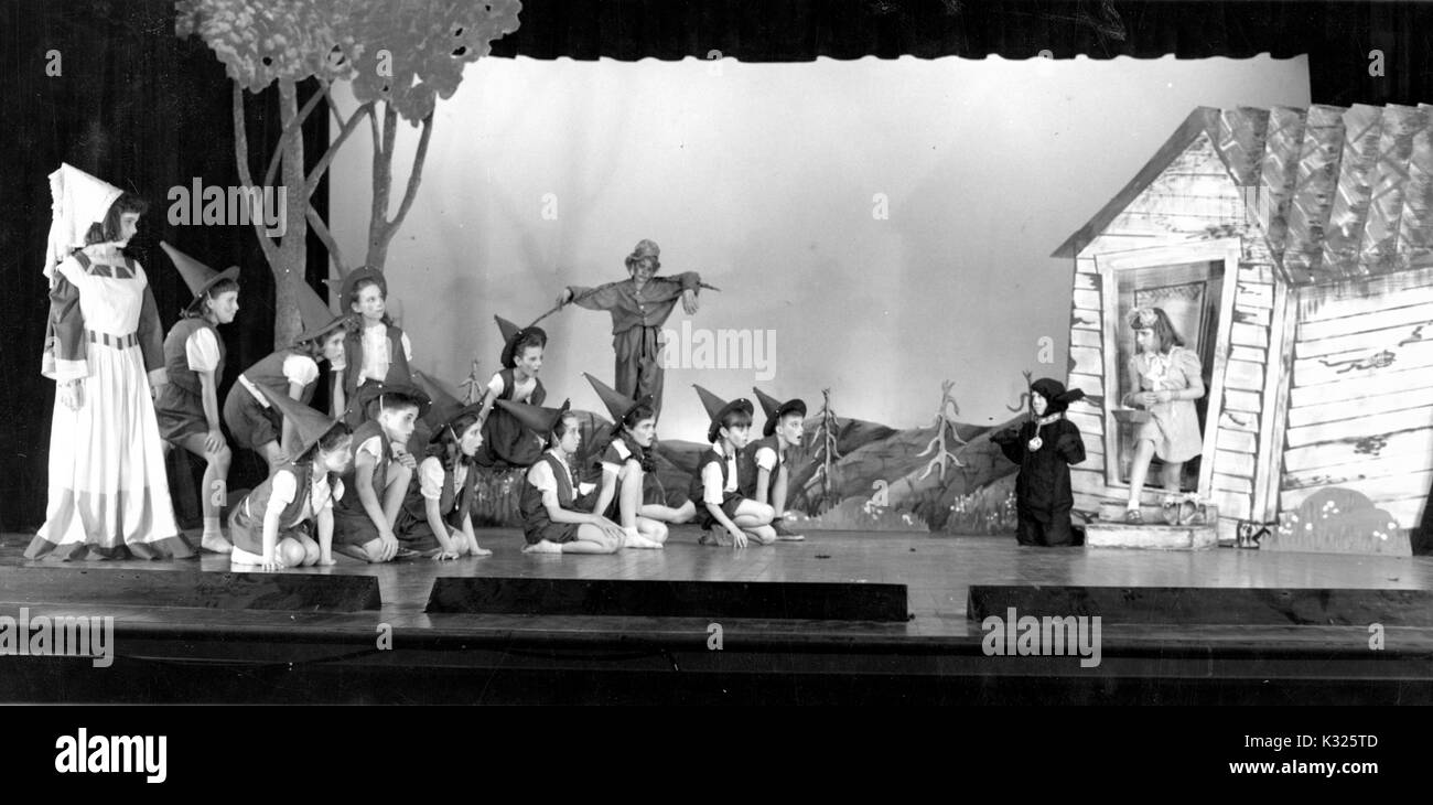 An eine elementare Demonstration school der Johns Hopkins University, Jungen und Mädchen, die auf eine Leistung von der Zauberer von Oz auf der Bühne in einem Hörsaal, mehrere hocken auf der Bühne tragen wies Hexe Hüte, mit einer Vogelscheuche, zwei Hexen, und der protagonist Dorothy, durch ein Bühnenbild, bestehend aus einem kleinen Haus und Bäume, Baltimore, Maryland, Juni, 1947 umgeben. Stockfoto