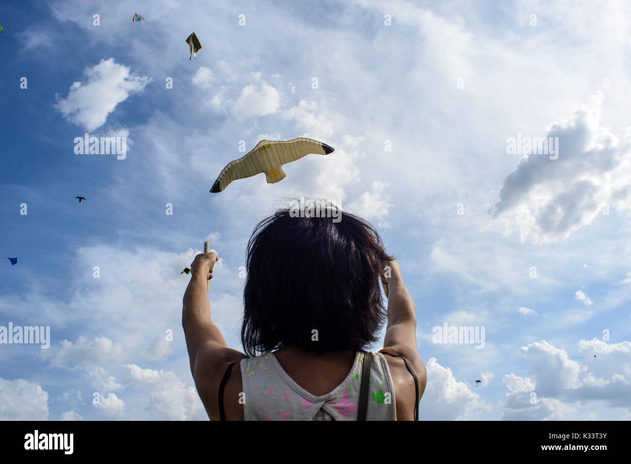 Eine Frau spielt mit einem Vogel-förmige Kite in den Wolken an einem sonnigen Frühlingstag Stockfoto
