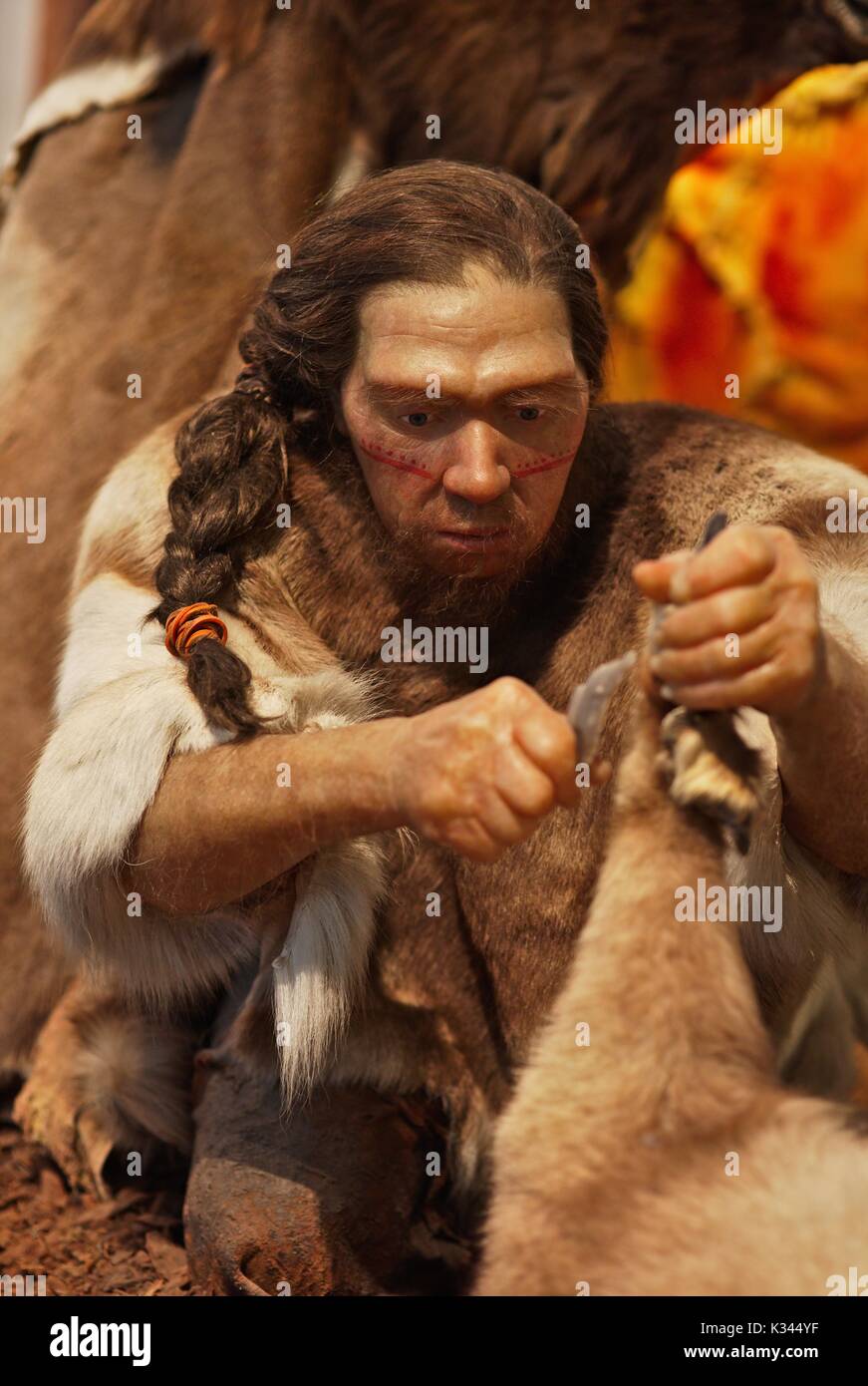 Der Neandertaler mit rotem Gesicht Farbe schneiden Beute, schneiden Bein mit einem Stein Messer Stockfoto