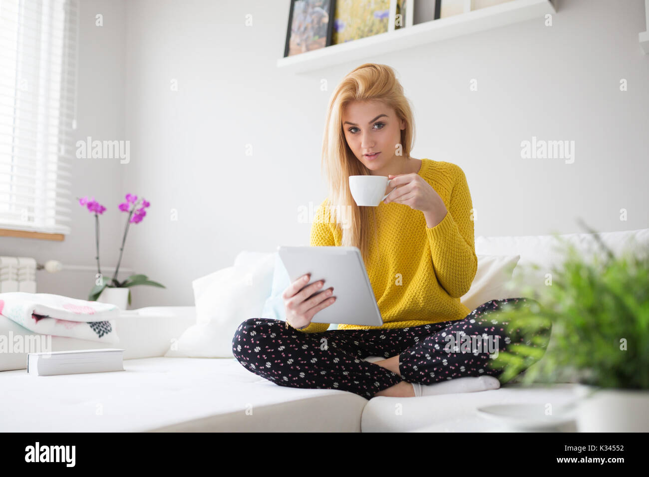 Ein Foto der jungen Frau im Schlafanzug Freizeit mit Tablet und einer Tasse Kaffee. Stockfoto