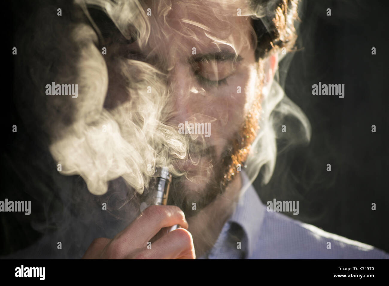 Junger Mann vaping Elektronische Zigarette, E-Zigarette, e cig mit Rauch Wolken. Stockfoto