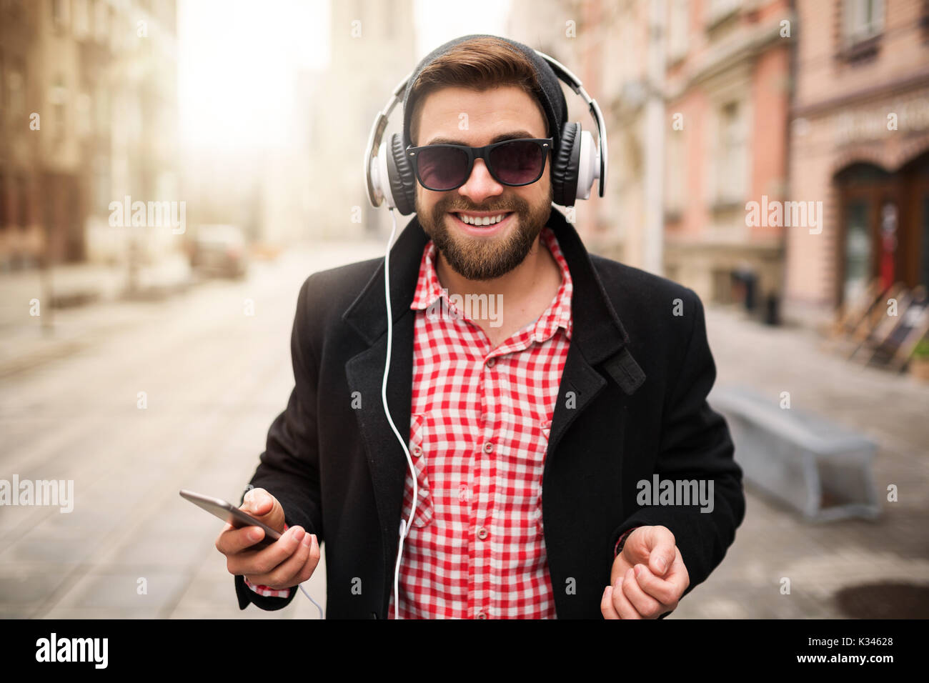 Ein Foto der jungen, trendigen Mann stand auf dem Marktplatz und die Musik durch weiße Ohrhörer. Er ist glücklich. Stockfoto