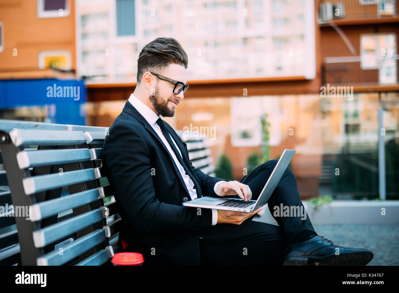 Geschäftsmanns, der mit seinem Computer und trinken Kaffee auf einer Bank Stockfoto