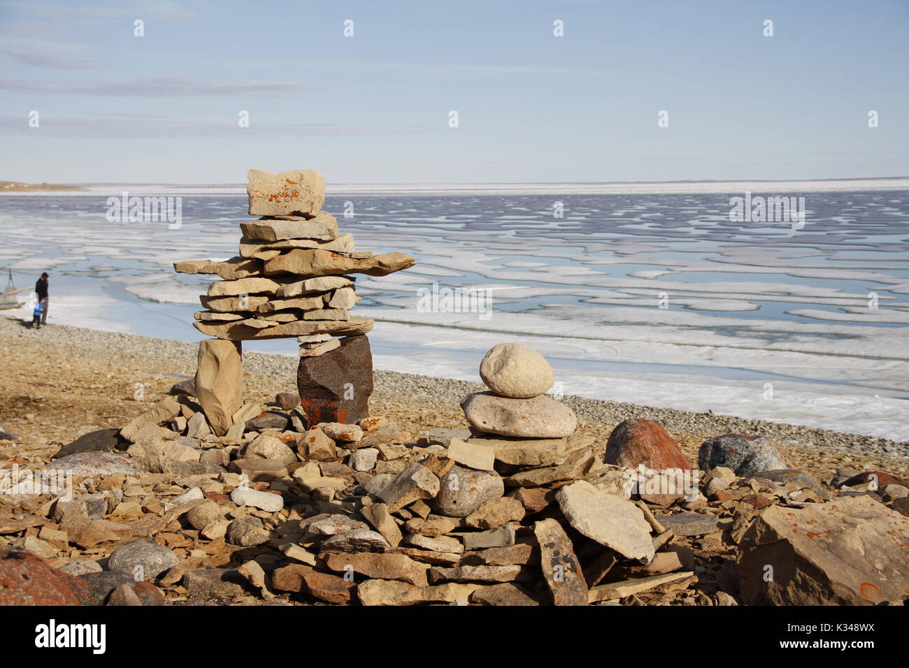 Inukshuk oder Inuksuk auf einem felsigen Strand mit Eis auf dem Ozean Ende Juni in der hohen Arktis in der Nähe der Gemeinde von Cambridge Bay Stockfoto