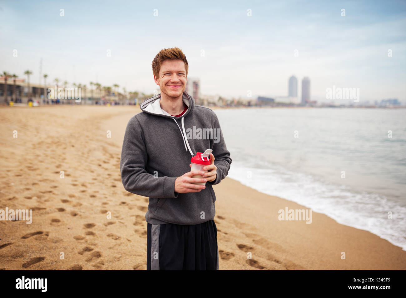 Ein Foto von junge, glückliche Menschen im sportlichen Outfit stehen auf dem Strand mit einem bidon in seinen Händen. Stockfoto