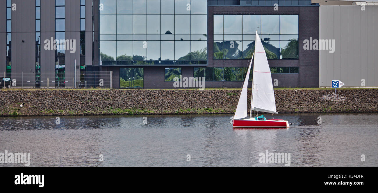 Rote segelboot segeln Vergangenheit a waterfront Bürogebäude Stockfoto