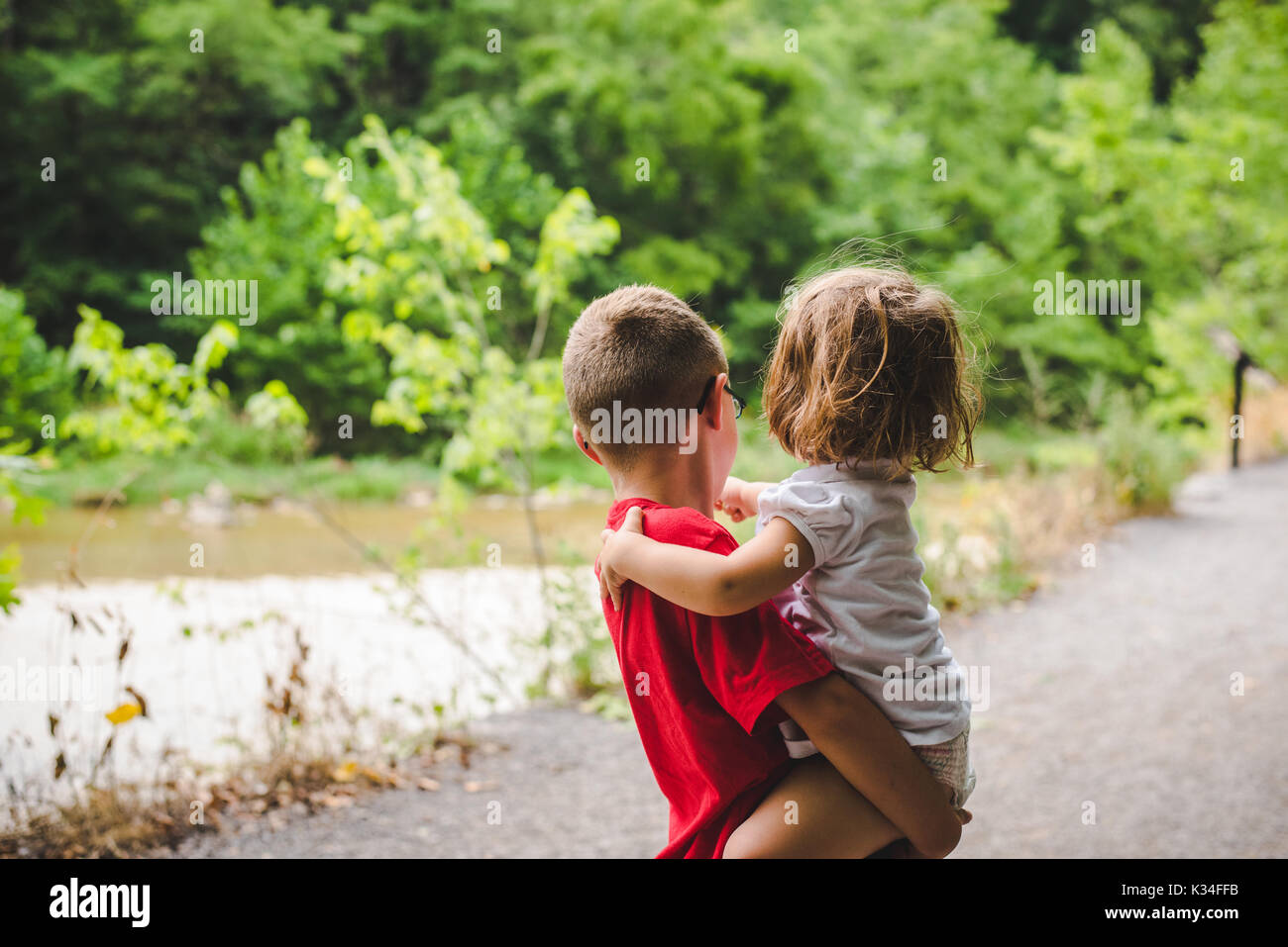 Ein kleiner Junge hält ein kleines Mädchen auf einem Pfad, der von Bäumen gesäumt. Stockfoto