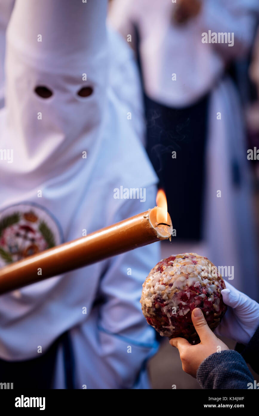 Einen Pönitenten von 'Los Negritos ' Bruderschaft tropfen Kerzenwachs auf eines jungen Wachs Kugel während der Semana Santa (Karwoche), Sevilla, Andalusien, Spanien Stockfoto