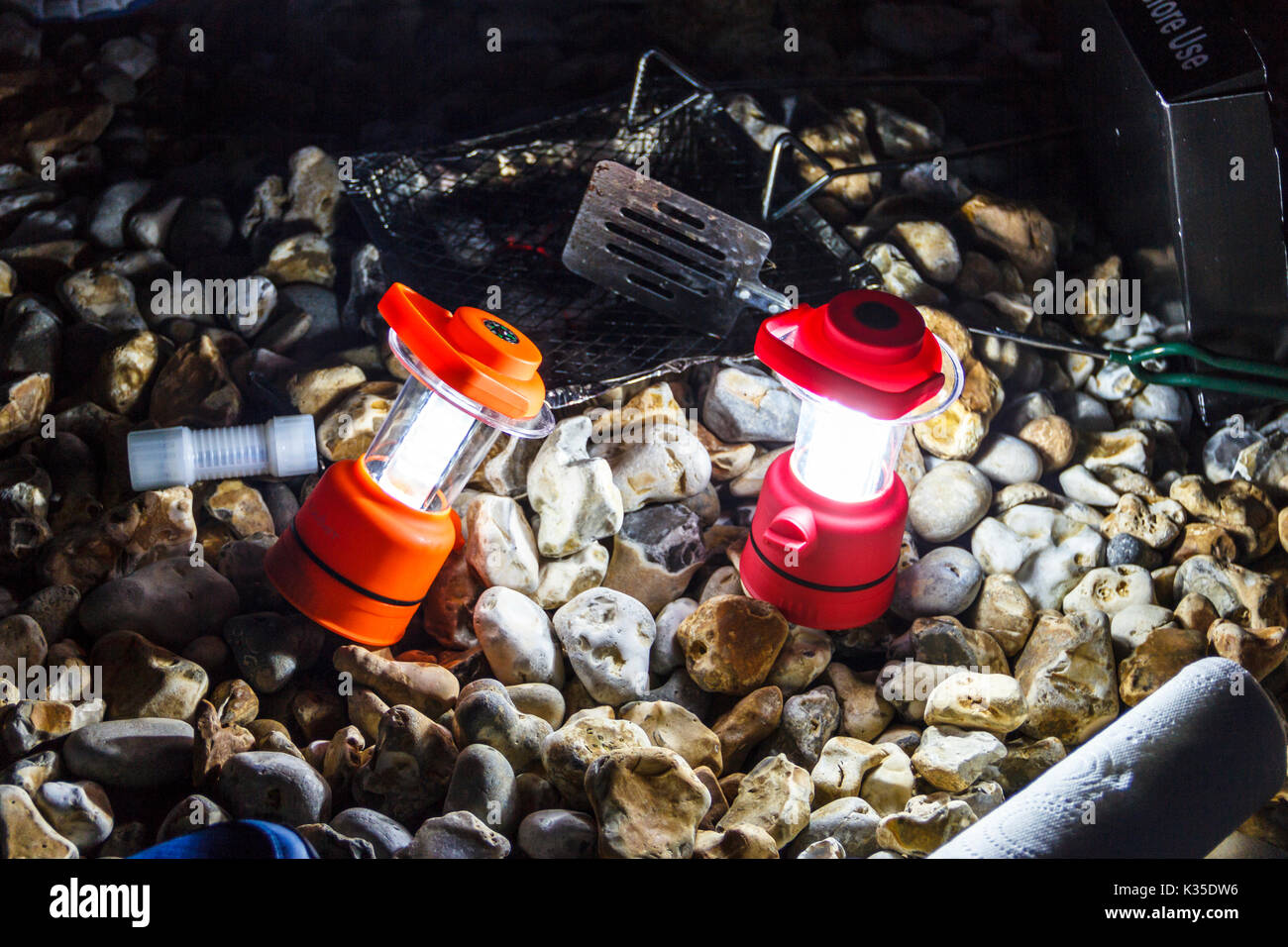 Close-up von zwei roten Camping Laternen beleuchten eines steinigen Strand bei Nacht, nach einem Grill Stockfoto