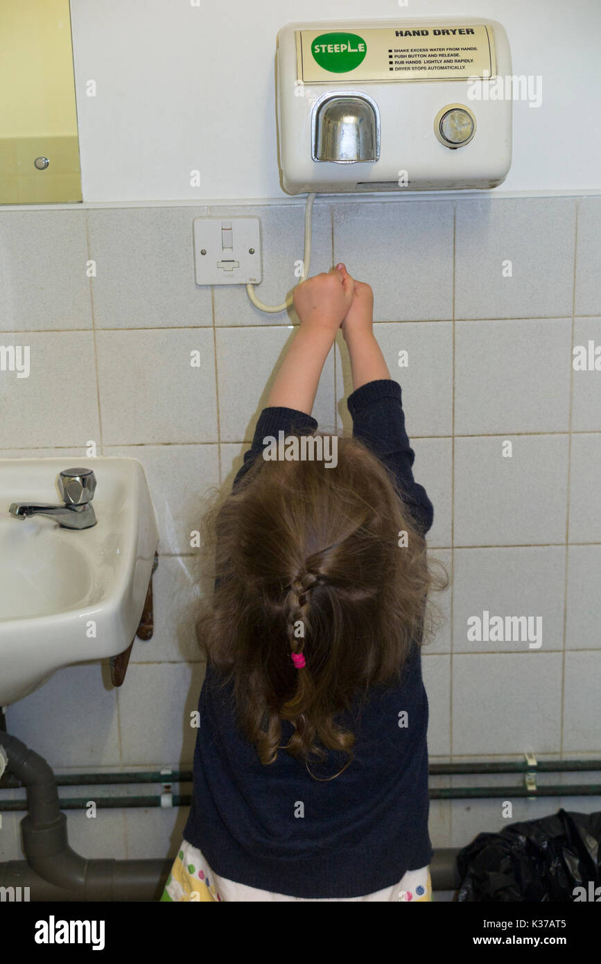 Junges Mädchen / Kind / 3 / 3 jährige trocknen trocknet ihre Hände mit einer Warmluft-Händetrockner in einer öffentlichen Toilette / Waschbecken / WC. UK Stockfoto