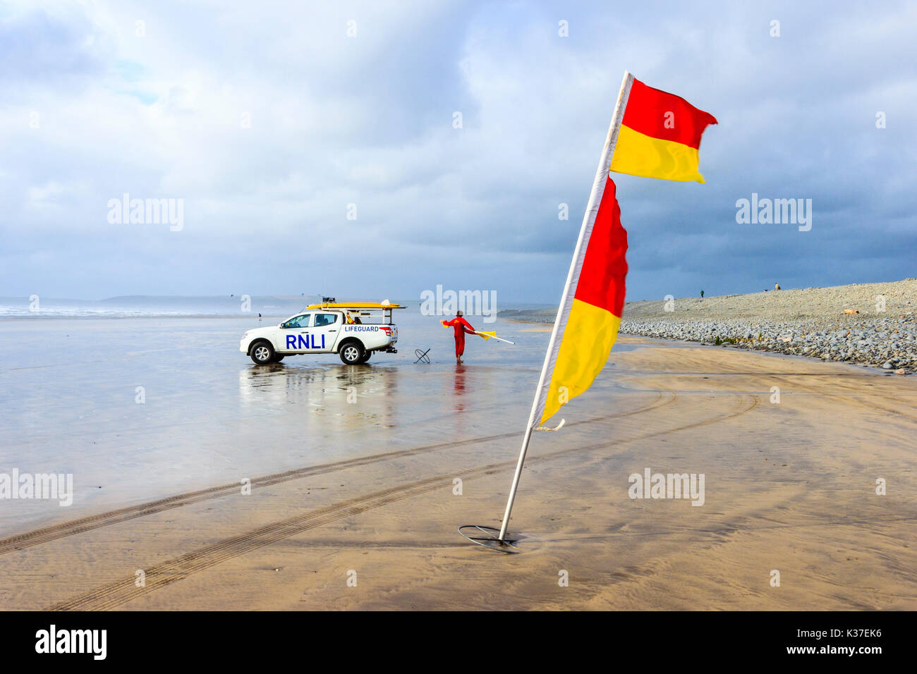Rot und Gelb Warnung Flagge und RNLI Rettungsschwimmer mit Fahrzeug auf dem sandigen Strand an der Westward Ho! Bei Ebbe an einem bewölkten und windigen Sommer Tag Stockfoto