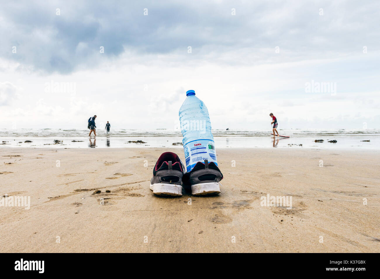 Low Angle Nahaufnahme einer Wasserflasche und Schuhe von einem Surfer auf einem sandigen Strand bei Ebbe links, Westward Ho!, Devon, England, Großbritannien Stockfoto