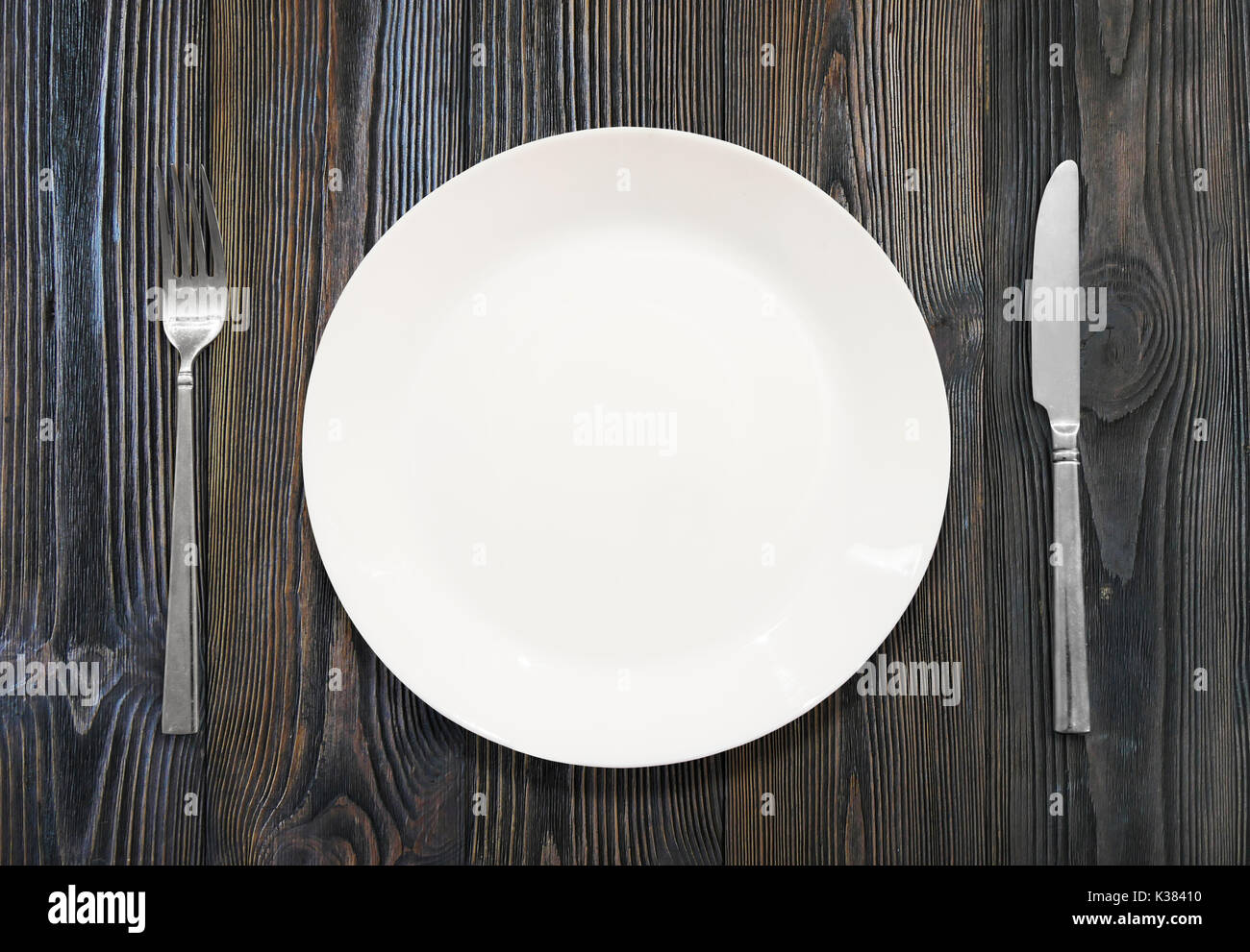 Weißer Teller, Messer, Gabel, auf einem Hintergrund aus Holz Stockfoto