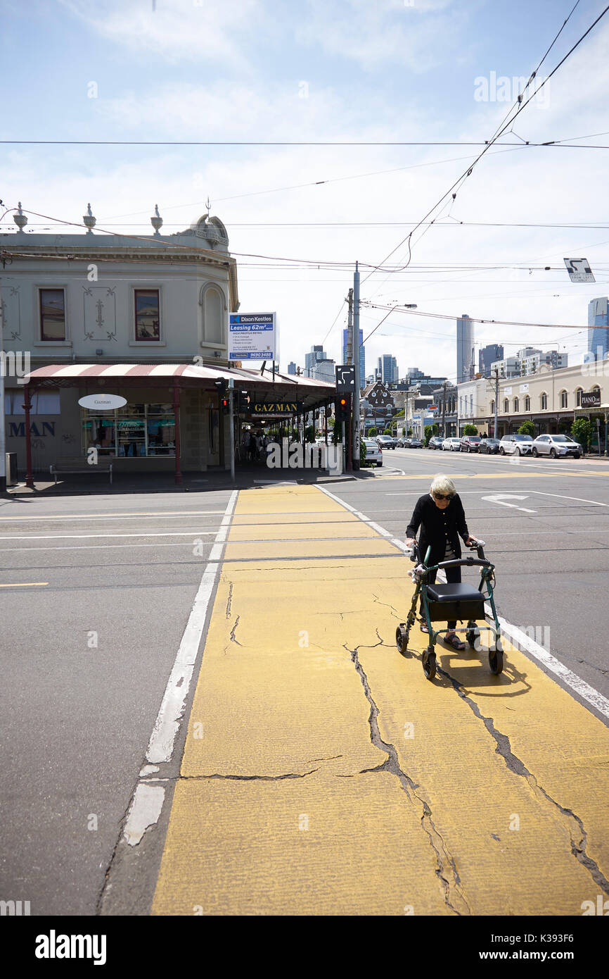 Alte Frau mit einem Walker überquert eine breite Straße in Melbourne, Australien Stockfoto