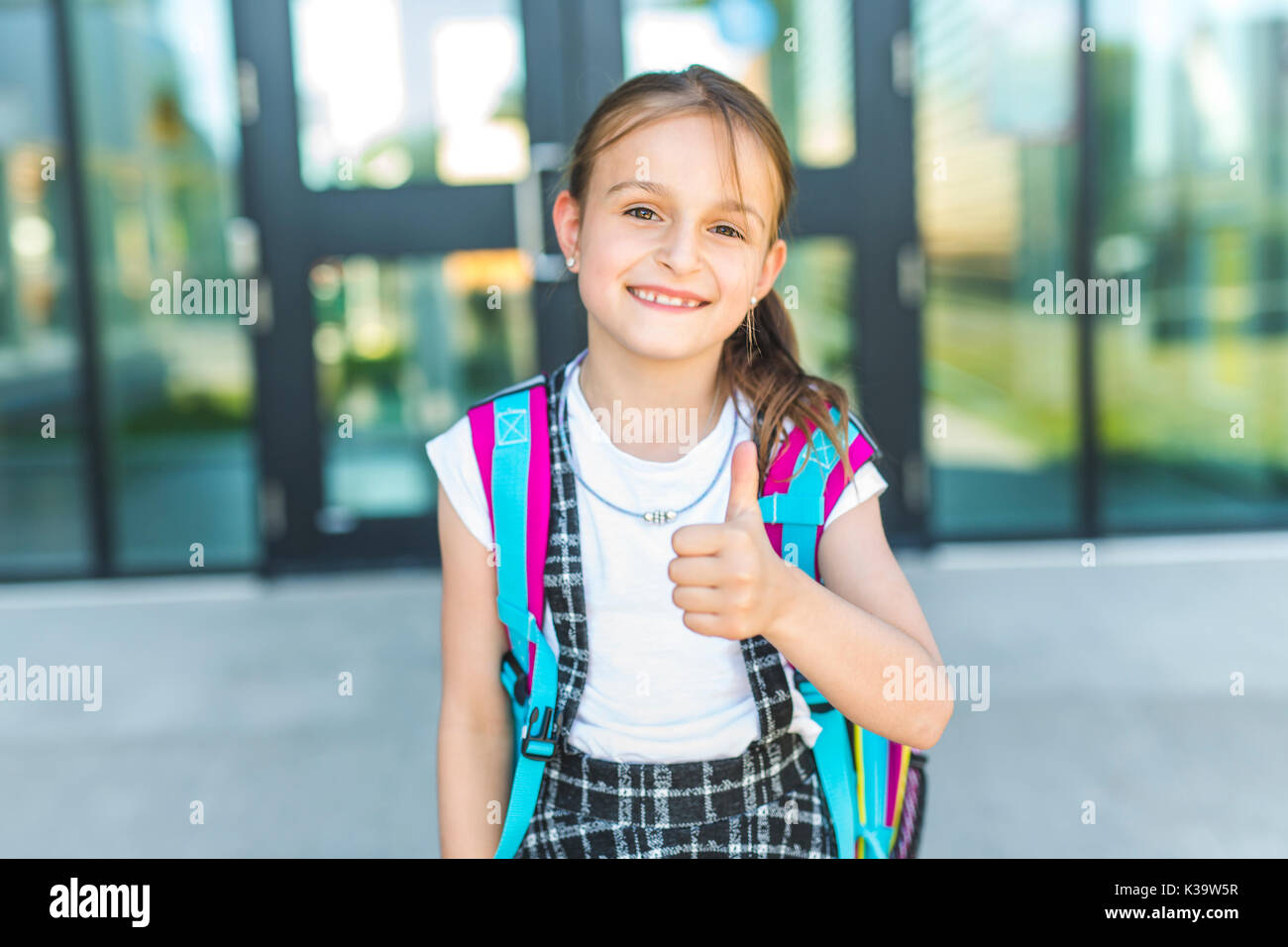 Mädchen außerhalb der Schule mit Tasche stehend Stockfoto