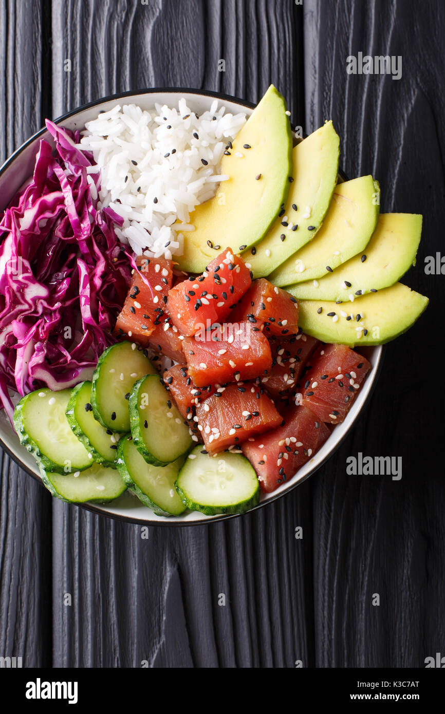 Hawaiian tuna poke Schüssel mit Avocado, Rotkohl, Gurken und Sesam auf schwarzem Holz- Hintergrund. Draufsicht von oben vertikal Stockfoto