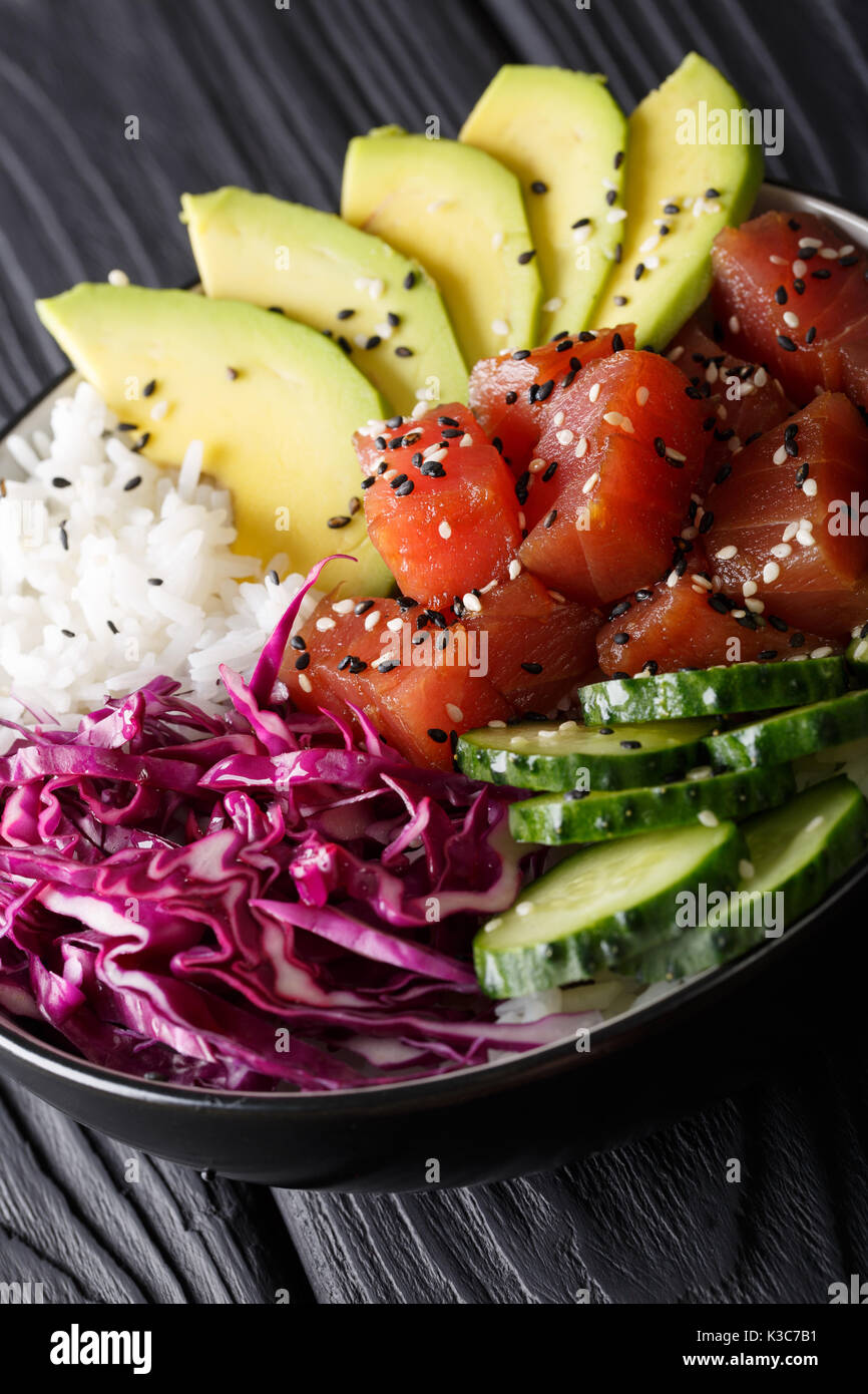 Hawaiian tuna poke Schüssel mit Avocado, Rotkohl, Gurken und Sesam auf schwarzem Holz- Hintergrund. Vertikale Stockfoto