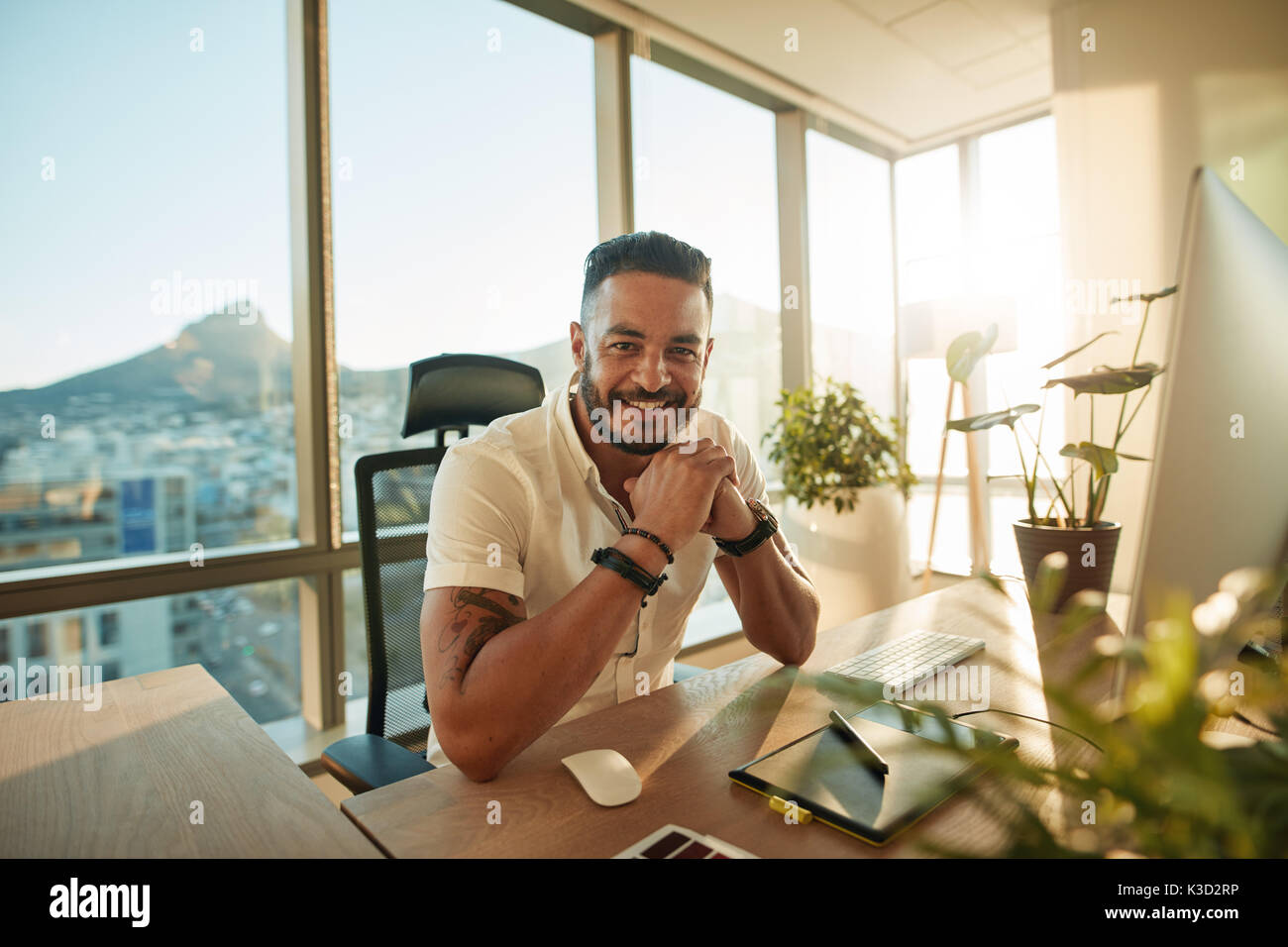 Portrait von kreativen jungen Mann im Amt. Männliche Designer an seinem Schreibtisch sitzt und lächelt. Stockfoto