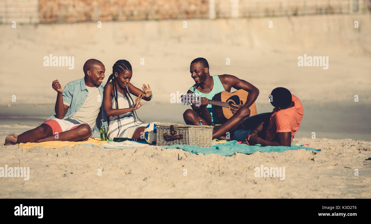 Gruppe junger Leute am Strand hängen. Junge afro-amerikanische Mann spielt Gitarre für Freunde. Stockfoto