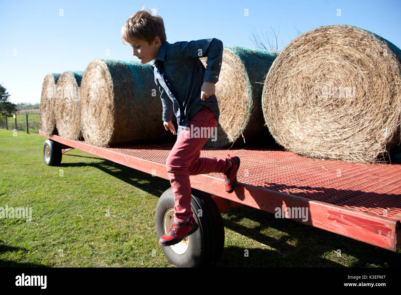 Junge springen die Seite einer Farm Traktor Anhänger mit Heuballen. Stockfoto