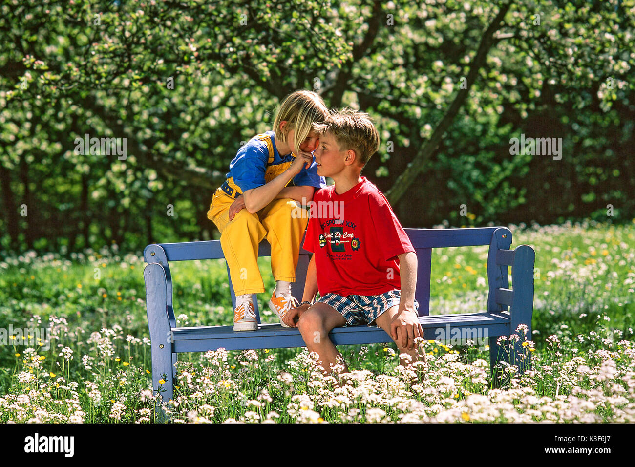 Mädchen und Jungen sitzen auf der Bank im Garten und Flüstern Stockfoto