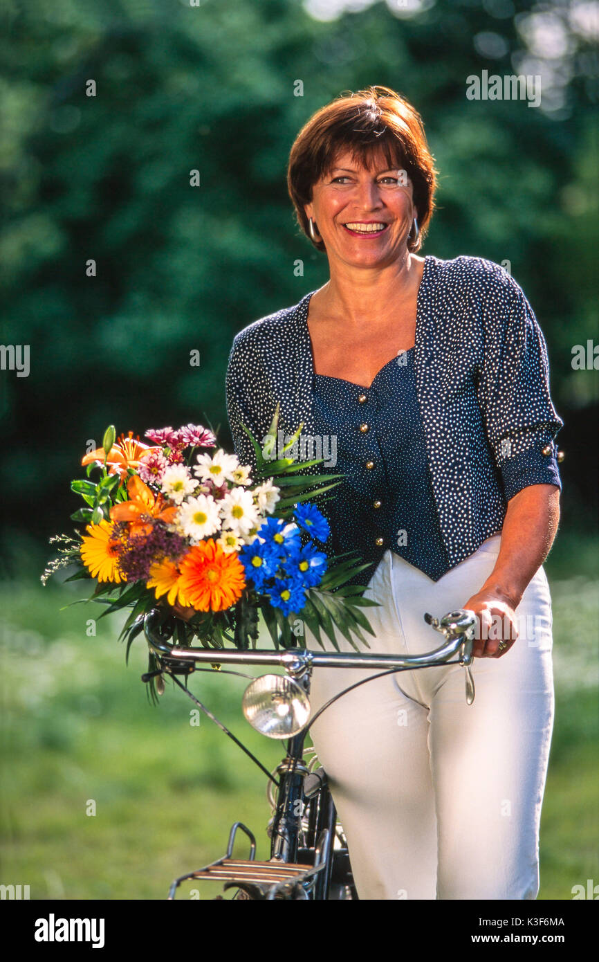Frau Räder ihr Fahrrad und hat einen Blumenstrauß in der Hand Stockfoto