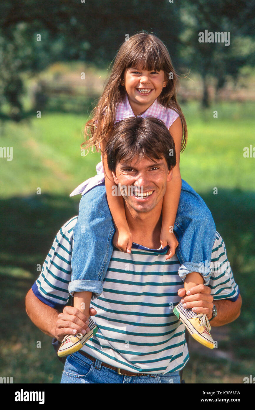 Vater trägt Lachen Tochter mit braunen langen Haaren auf den Schultern Stockfoto