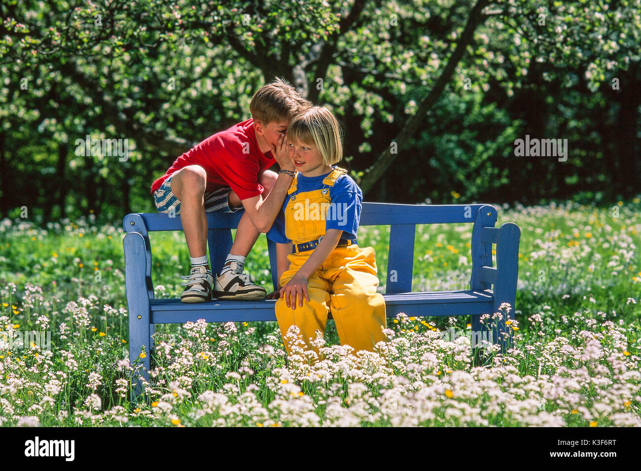 Mädchen und Jungen sitzen auf der Bank im Garten und Flüstern Stockfoto