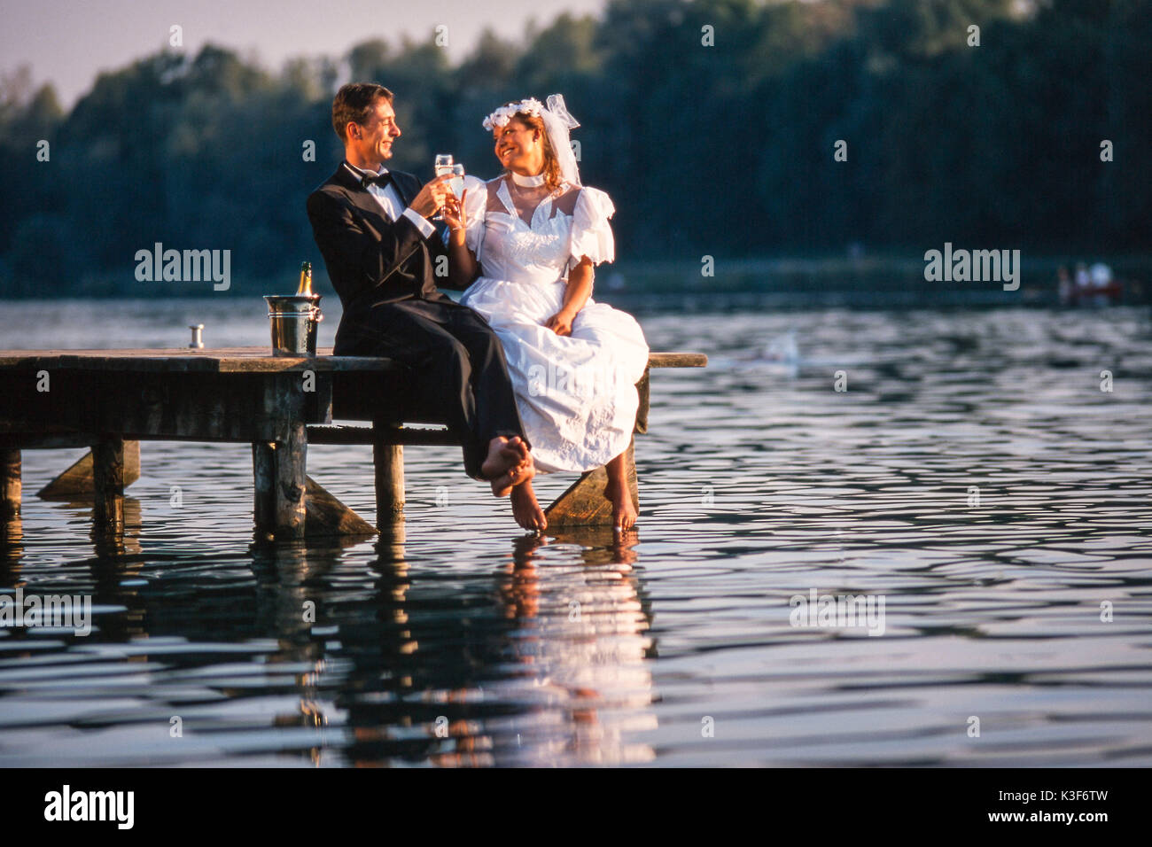 Brautpaar sitzt auf der Brücke mit Champagner Glas in der Hand Stockfoto