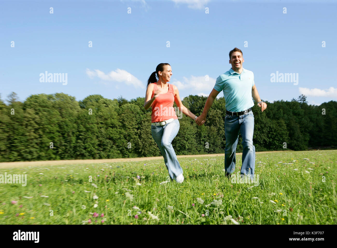 Junges Paar läuft Hand in Hand über einer Wiese Stockfoto